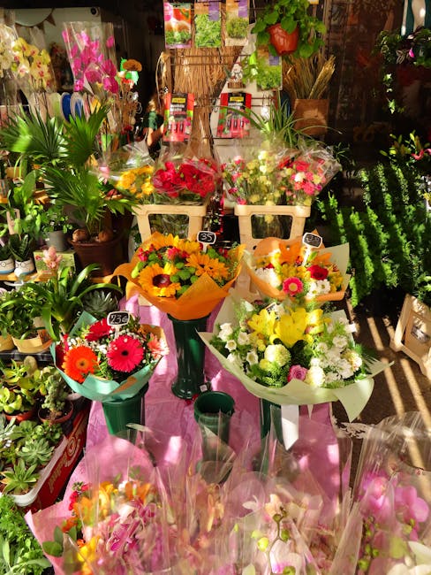 A vibrant display of fresh flower bouquets arranged on a pink table inside a florist shop. The bouquets feature a variety of flowers, including bright yellow sunflowers, cheerful pink gerbera daisies,